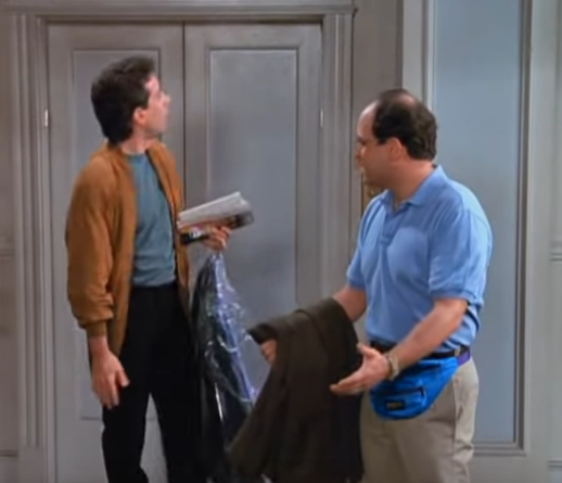 Sort of dumpy looking guy in a blue golf shirt wearing a bright blue fanny pack, talking to a guy wearing what looks like a 1980's style jacket with big hair, green shirt and black slacks, inside an apartment of some sort