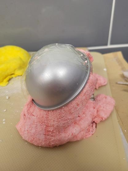 Gooey pink mess, sitting on a textured surface. Looks a bit like a sloppy scoop of icecream. It has a metal semi-circle sitting on top.