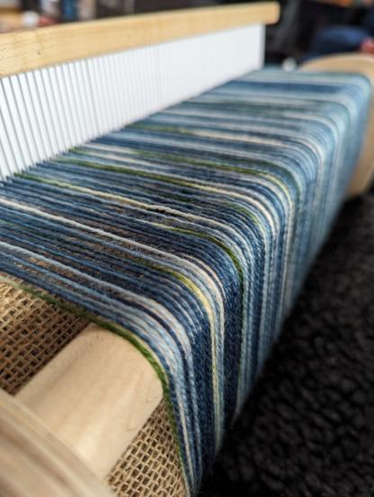 The edge of my rigid heddle loom showing the pretty blue/green/white variegated yarn I'm using as warp this time.