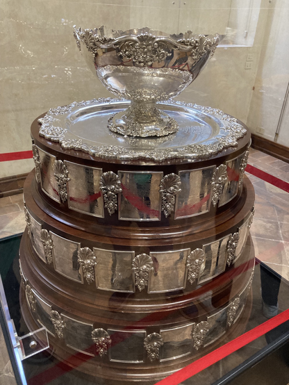 L’immagine ritrae il trofeo della Coppa Davis in metallo prezioso sistemata su un piedistallo in legno con placche in metallo con i nomi delle squadre vincenti