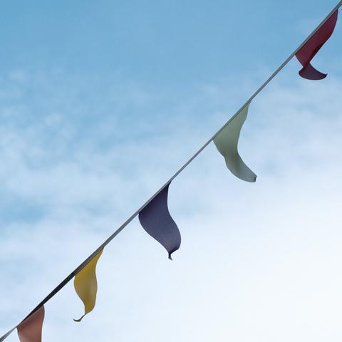 Colorful flags strung up on a line fluttering in the wind, with a backdrop of a soft blue sky and wispy clouds.