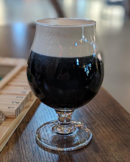 Black beer in a glass snifter with a wooden Shut the Box game beside.