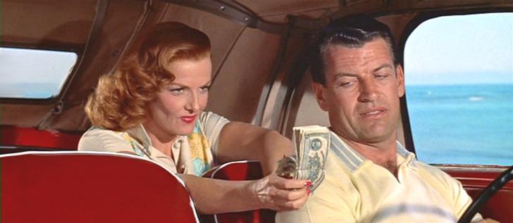 a man with greying hair who is driving a car turns back to look at a curvaceous woman with red hair in the back seat, who is showing off a large stack of money