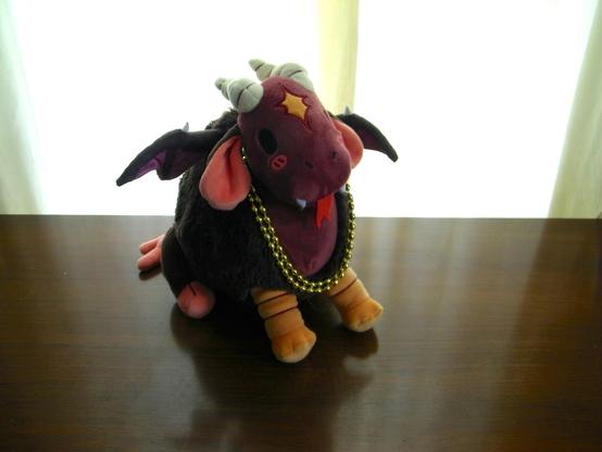 A red and brown plush with white horns, orange feet, and brown bat wings -- wearing a couple of gold necklaces.