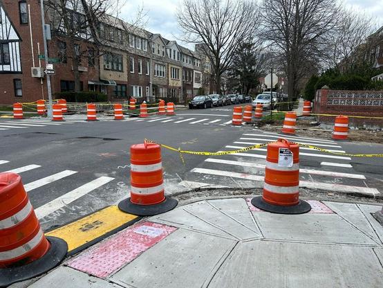 At three of the four corners of the intersection of Dartmouth Street and 68th Avenue in Forest Hills, curb cuts are being made ADA-accessible.  They have been repaved, but there are still trenches next to the curb, marked by orange barrels and yellow caution tape.