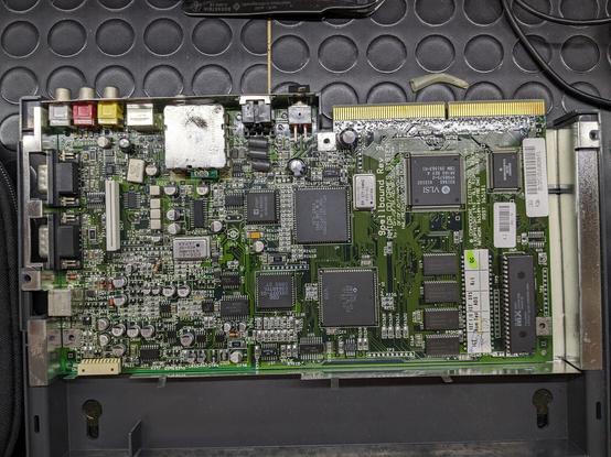 Photo from above of a CD32 motherboard still in the case, but with the shielding removed. The board seems to be relatively clean, but two caps near the expansion port are bulging.