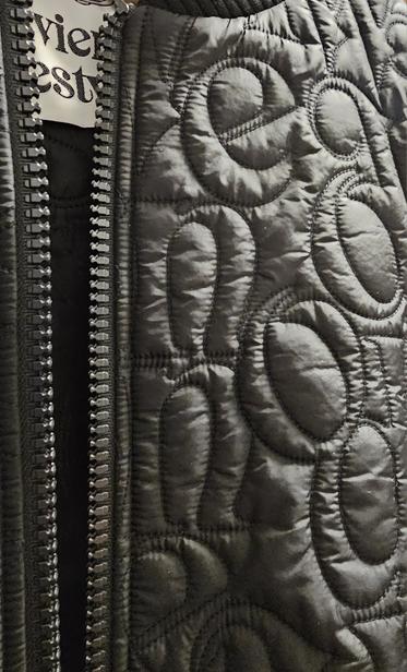 Close-up photo of a black jacket zip and material, showing stitched letters e, n, o and part of a Vivienne Westard brand label