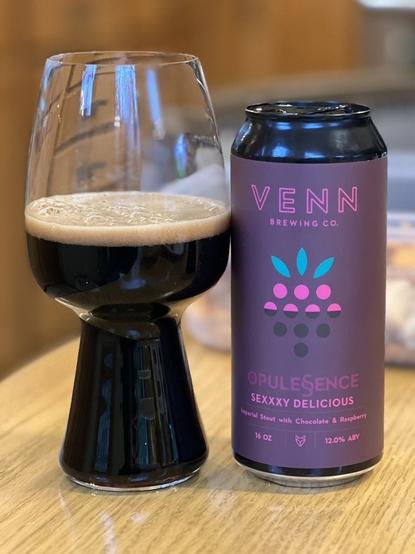A half full stout glass is to the left of a pint can from Venn Brewing. The can label is dark purple with a red and green raspberry styles graphic