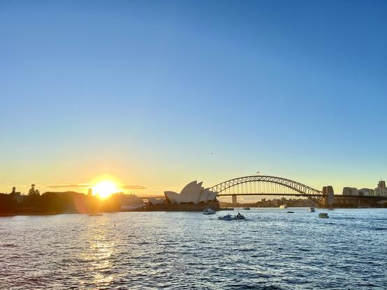 Bright orange sun setting behind the silhouette of Sydney CBD, the iconic shapes of the Opera House and Bridge