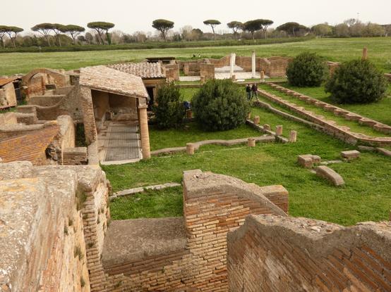 A peristyle courtyard, with adjacent buildings, one with a fine mosaic, amongst the grass and trees of ancient Ostia.