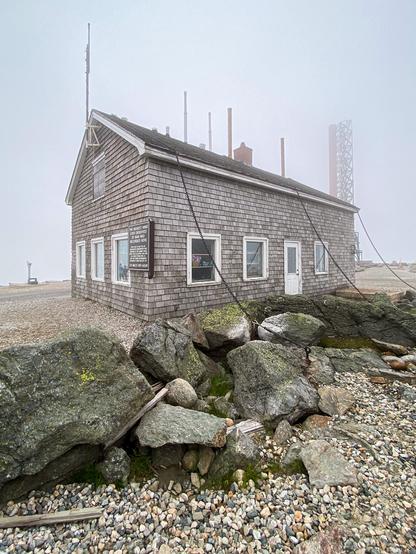 Color photo of a wood building being held down  by 3 heavy chains on the summit of a very windy Mt Washington.