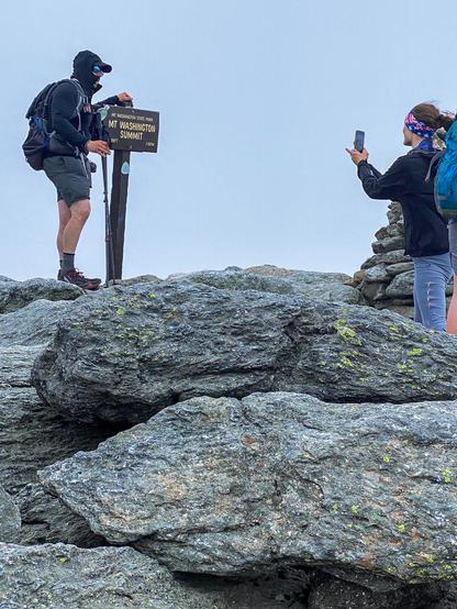 Color photo of a hiker standing next to this sing at the summit  having a photo taken.     Saw quite a few hikers at the summit.