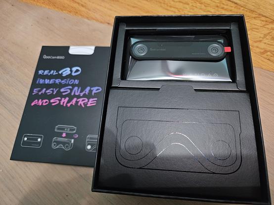 The inside of the box for the Kandao QooCam Ego. There is an insert with the text "Real 3D Immersion, Easy Snap and Share". The QooCam Ego is inside the box itself with dual camera lenses pointed upwards.
