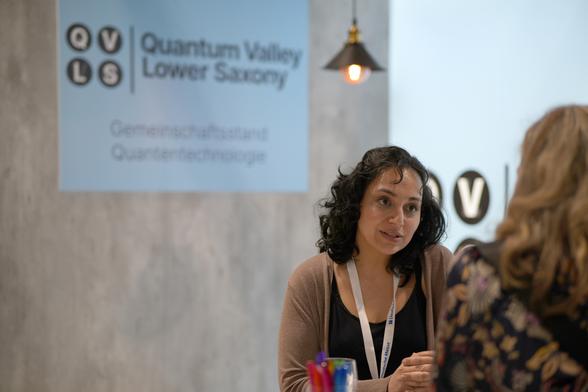 Zwei Menschen im Gespräch vor einem Plakat des Quantum Valley Lower Saxony. Foto: QVLS