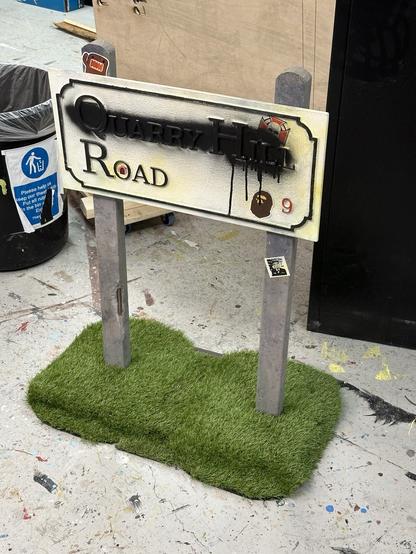 Same sign only now the top line is made unreadable by spray paint. The wooden base has embedded castors and is coved in astroturf.