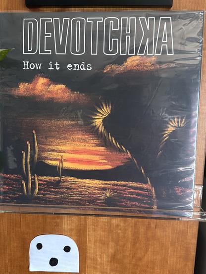 Cover to How it ends by the band Devotchka. Features a painting of a desert sunset with clouds and cacti.