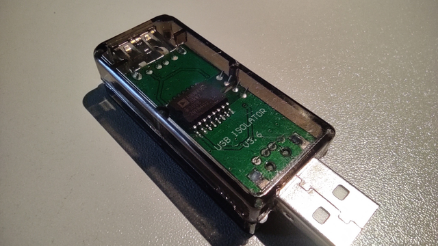 In the photo, there's an electronic circuit board with a USB-A plug, housed in a dark translucent casing with rounded, smooth edges. The label 'USB ISOLATOR v3.6' is clearly visible.
