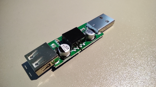 In this photo, the circuit is seen removed from the dark translucent casing, with a USB-A plug visible - male on one side, female on the other. In the center, between them, is a voltage converter surrounded on both sides by electrolytic capacitors labeled 'gs 220 6.3v.' Also visible are other surface-mount passive components.