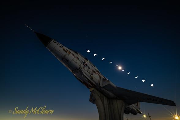 Composite image of eclipse phases over a 1950s jet fighter gate guardian.