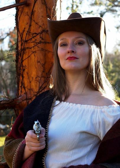 Foto entnommen vom Twitteraccount von Wolfram Christ (Veranstalter)
Es zeigt eine Frau mit langen Haaren im cowboyoutfit. Hut weiße Bluse, braunes Cape und Pistole