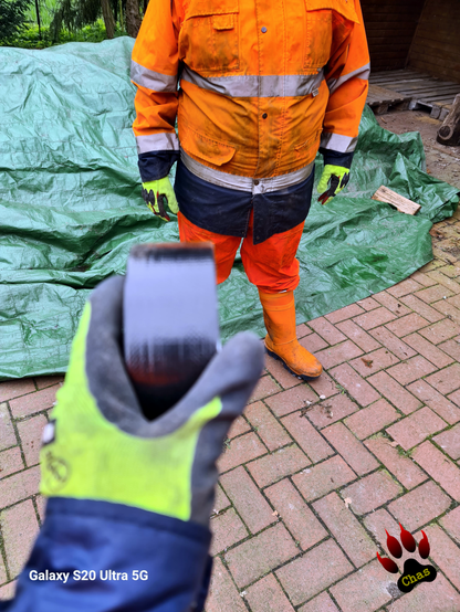 torso picture of person wearing hi vis raingear and orange rubber boots. in foreground another hand holding a roll of duct tape amied at aformentioned person