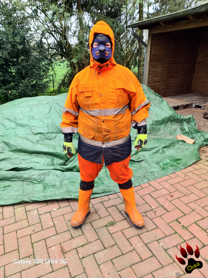 human pup, wearing hi vis raingear, rubebr boots and gloves, standing in front of a pile of firewood (covered by plastic canvas); gloves and boots secured with black duct tape