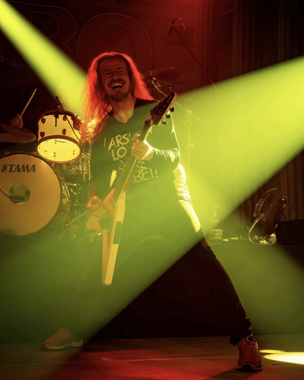 Vito rockt auf der Bühne, die Flying-V in der Hand und grinst.