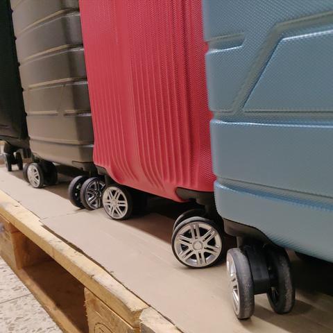 Die unteren Hälften von drei Hardshell-Trolleys in schwarz, rot und grau-blau, mit unten angesetzten Beinchen mit Plastikrädern.