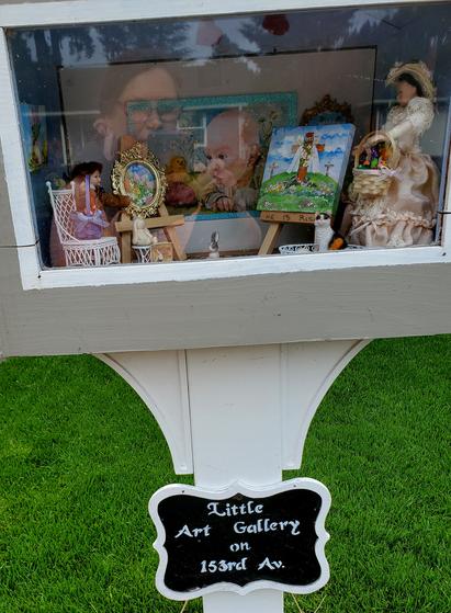 A glass fronted box sits at eye level on a post. Behind the box's window is a miniature artist's studio with a Victorian theme.