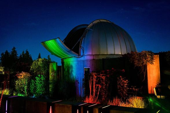 Exterior shot of the Trottier Observatory at night, lit up with the spectrum of the sun.