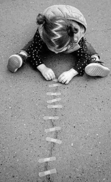 Kind sitzt auf Asphalt und klebt einen Riss darin mit Pflastern zu

Foto: Pinterest