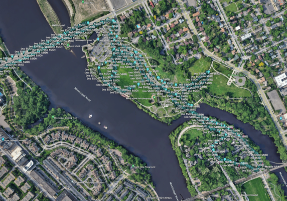 An image of a map showing Boom Island and Nicollet Island in Minneapolis, MN. Overlayed on the map are blue balloons by the thousand, each representing on BlueTooth device.  Captured with a JHewitt revision 5G wardriving rig.