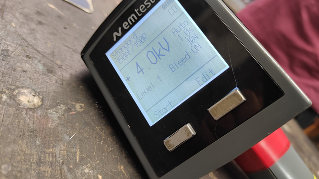 The ESD gun display, EM Test brand, shows the following:

On the left: Standard 150pF/150R
On the right: Icon of a full battery and 'CD'
In large letters: '+4.0kV' next to 'Auto 1.0s', '10', and a down arrow
Below: 'Level 1 Bleed ON'
At the bottom: 'Start' and 'Edit' above the buttons, explaining their functions.