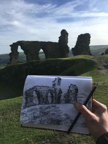 Photo showing charcoal drawing of Dinas Bran Castle ruins with Dinas Bran in background to show it was drawn on location in plein air