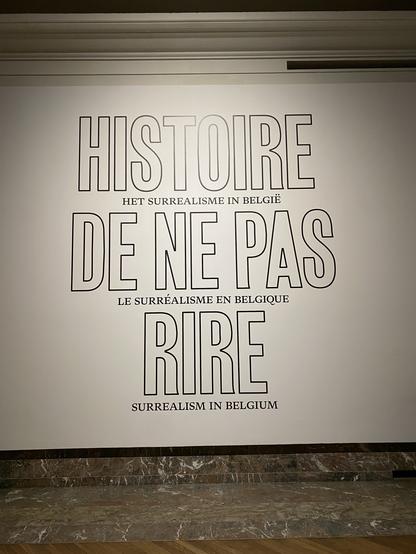 Photo d’un mur blanc avec des lettres énormes: « Histoire de ne pas rire, le surréalisme en Belgique » — une exposition au Bozar à Bruxelles