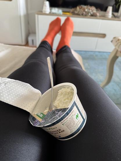 Ich liege halb auf der Couch und ein körniger Frischkäse in Schachtel mit Löffel liegt auf meinen Beinen
