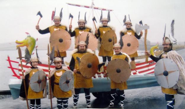 A picture of the 1978 Bressay up helly aa Jarl's squad a bunch of men and boys dressed up as comedy vikings on or in front of a model ship on a trailer.