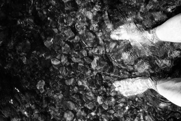 Feet in the water of a river, pebbles