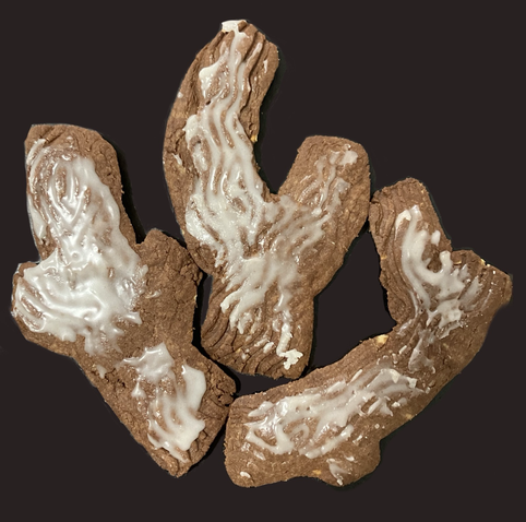Three cookies shaped like branches and textured with wood grain, iced with white icing to enhance the grain.