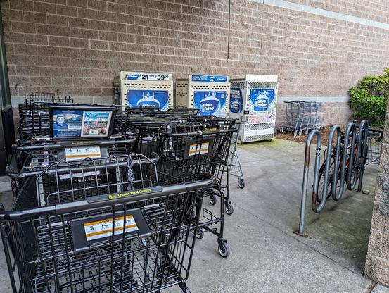 A badly placed cycle rack at QFC in Northgate, Seattle. There's not enough space between the rack and the wall, and the passage to it is almost blocked by the carts overflown out of the cart corral.