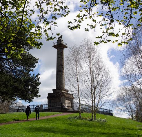 Large sandstone column in parkland with lion on top and a couple walking towards it