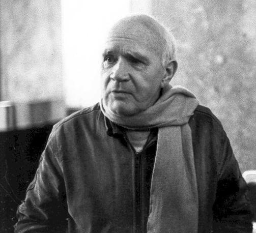Jean Genet in 1983, balding and wearing a scarf. By International Progress Organization - http://i-p-o.org/genet.htm, CC BY-SA 3.0, https://commons.wikimedia.org/w/index.php?curid=8499473