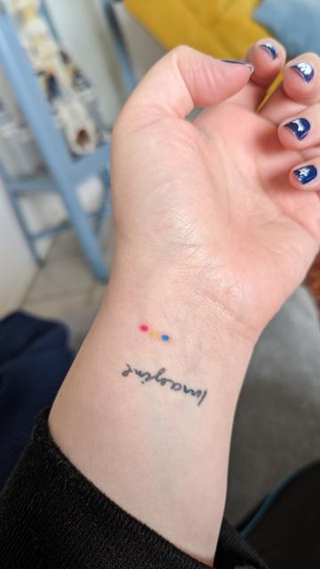 Meine Hand mit dunkelblau lackierten Nägeln. Am Handgelenk ist der Schriftzug "Imagine" in der Handschrift von John Lennon zu lesen und darüber befinden sich drei Punkte, die einen leichten Bogen beschreiben. Farben von links nach rechts: Pink, Gelb, Blau.