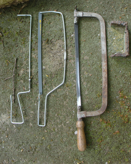 Three hack saws lying on a mossy stone: the rightmost is a big and heavy one. The middle is made out of wire, and the one on the left is a differently bent wire. It also doesn't have a blade.