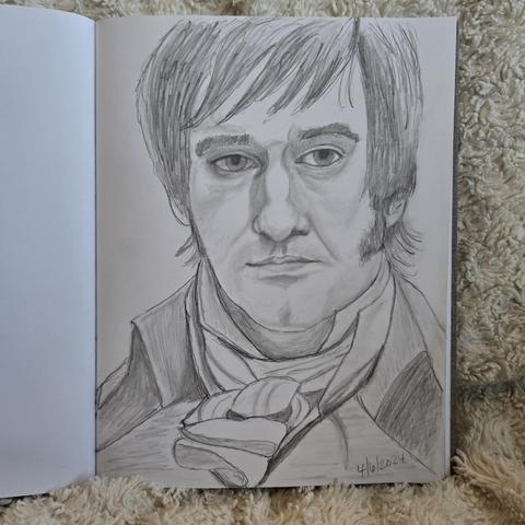 A sketchbook is open to a pencil sketch of Matthew MacFadyen as Mister Darcy from the 2005 adaptation of Pride and Prejudice. His bangs are long and swept to the side, and his sideburns cover the sides of his face. He wears a high collared shirt, a high collared waistcoat, a scarf tied in a knot around his neck, and a high collared coat. He looks at the viewer with a slightly bored, haughty look.