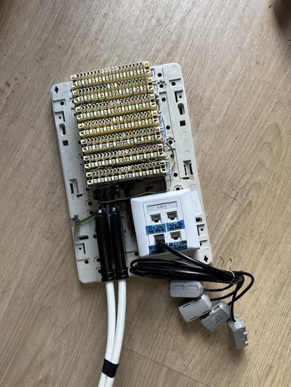 7 krone type punch down termination blocks, with a pair of large white cables terminated on plugs at the bottom of the case.  To the right is a square white faceplate with 4 RJ45 sockets, one of which had a black cable connected, with each core broken out to a BT Phone socket