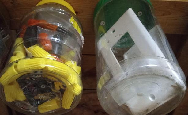 Two clear plastic jars. One full of various tiny electrical connectors, the other, spare light switch plastic face plates