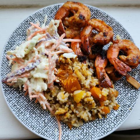 A plate of food. Barbecued prawns, a bit of coleslaw salad and some rice with pumpkin.