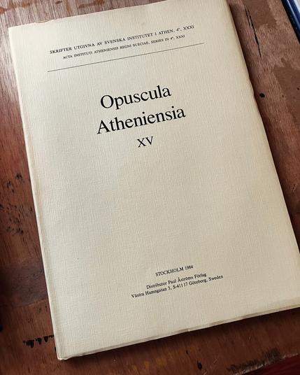 An academic journal titled "Opuscula Atheniensia" with a plain, pale yellow cover lies on a wooden desk.