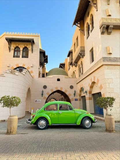Bright green Volkswagen Käfer in front of beautiful sand-colored buildings of the city of Sahl Hasheesh, Egypt